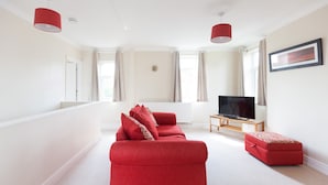 A spacious living room with a red sofa, a television, and a red ottoman. - Toothbrush Apartments - Ipswich East - Cauldwell Ave (Ipswich)