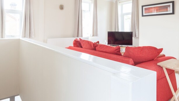 A modern living room with a white sofa, red cushions, a flat-screen TV, and a red pendant light. - Toothbrush Apartments - Ipswich East - Cauldwell Ave (Ipswich)
