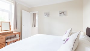 A bedroom with a large bed, a wooden dresser, a mirror, and two wall art pieces. - Toothbrush Apartments - Ipswich East - Cauldwell Ave (Ipswich)