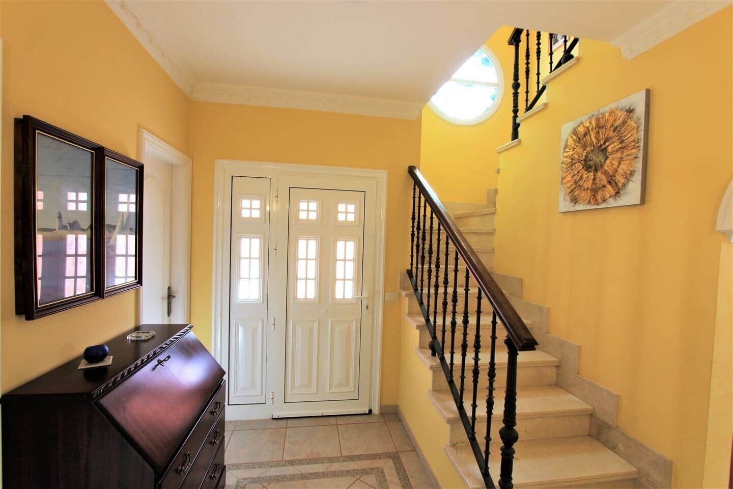 Un couloir avec un escalier, une commode et une porte.