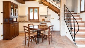 A kitchen with a dining table and chairs, wooden cabinets, a window, and a staircase. - Agriturismo Il Borghetto (Todi)