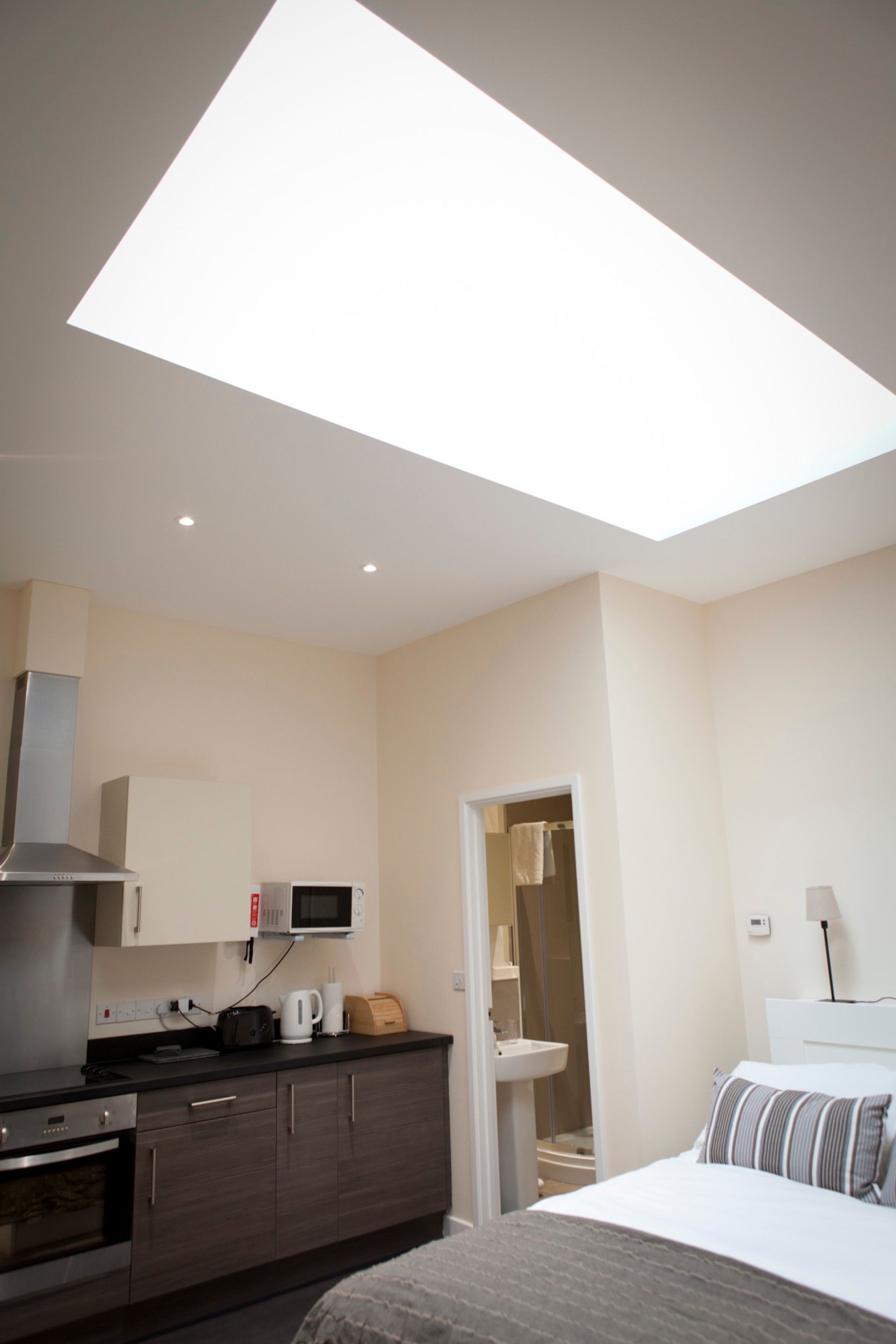 A modern hotel room with a skylight, kitchenette, and a bed with a striped pillow.