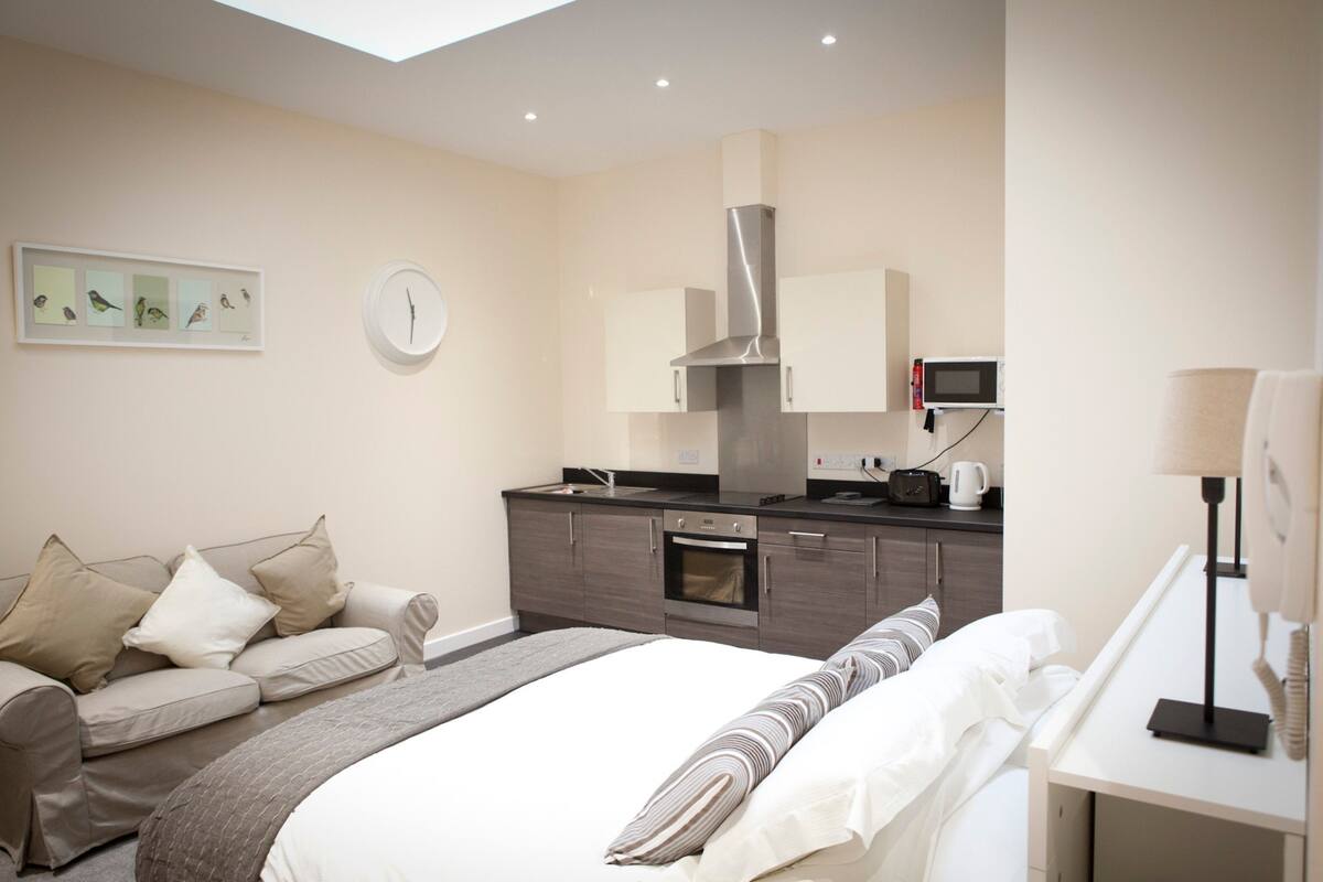 Una habitación de hotel moderna con cama, sofá, kitchenette y un reloj en la pared.