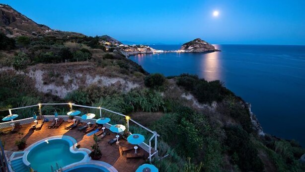 A pool area with lounge chairs and umbrellas, overlooking a coastal landscape with a moonlit sea and distant islands. - Torre Sant'Angelo (Forio)