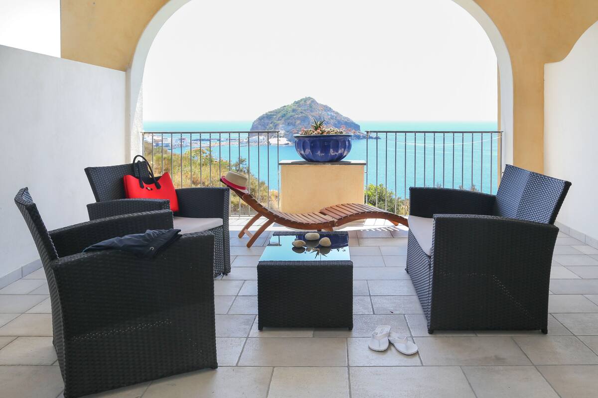 A balcony with wicker furniture, a red bag, and a blue pot with plants.