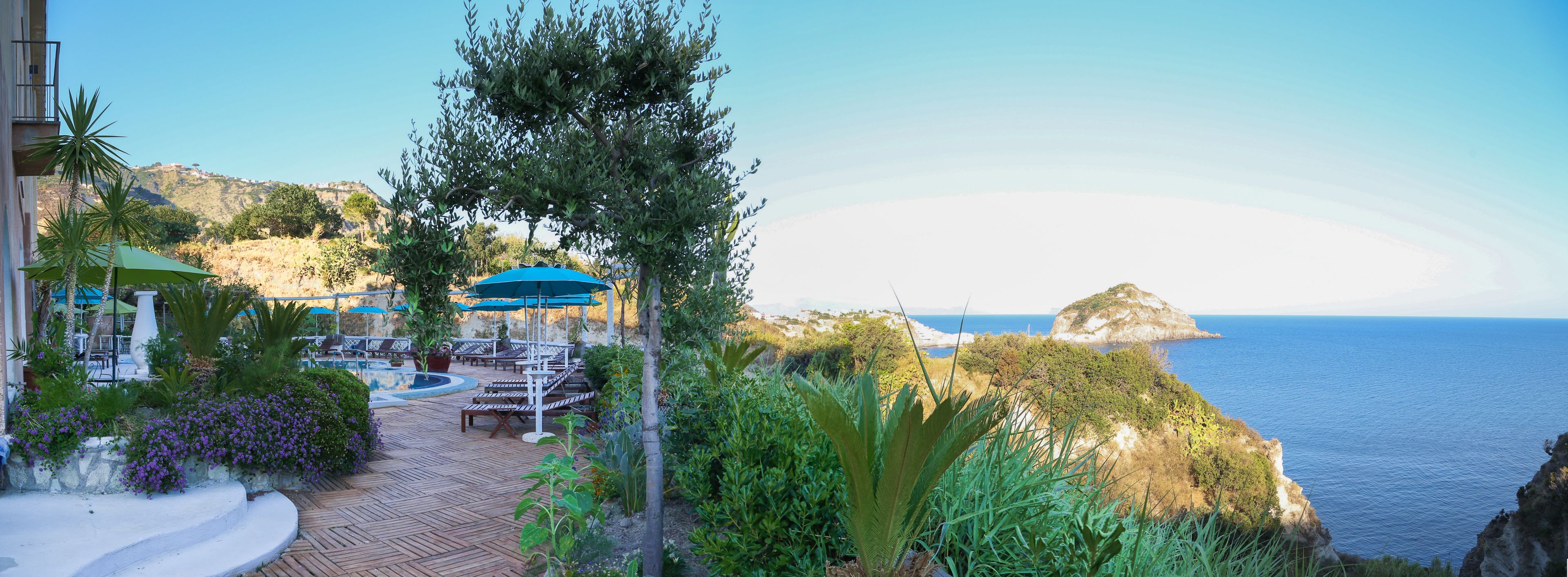 A wooden deck with lounge chairs and umbrellas overlooking a coastal area with a view of the sea and a small island.