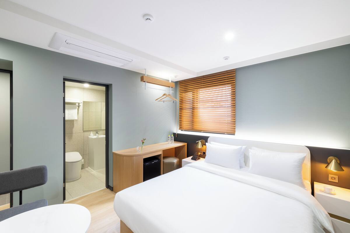 A modern hotel room with a bed, bedside table, lamp, and a view of the bathroom.