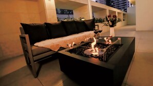 A modern outdoor seating area with a sofa, a glass-top table with a built-in fire feature, and a vase with flowers. - H-AVENUE Hotel Seomyeon Station (Busan)