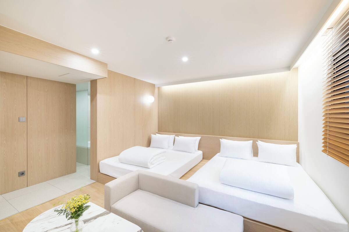 A modern hotel room with two beds, a sofa, and a small table with a vase of flowers.