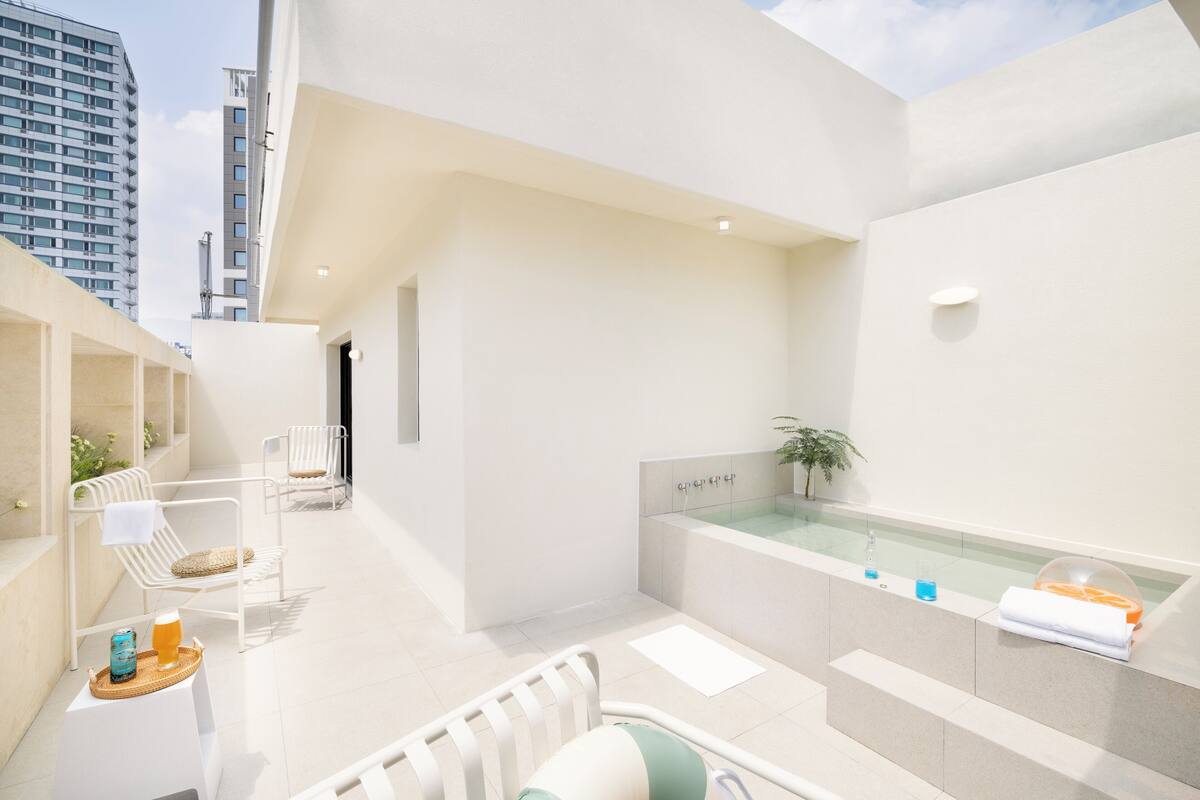 A modern bathroom with a bathtub, a small seating area with chairs, and a glass-enclosed shower.