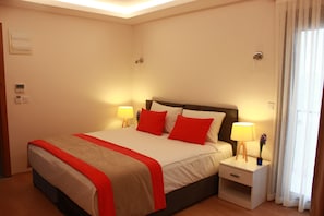 A neatly made bed with red and white bedding, two bedside lamps, and a nightstand with a lamp. - Imerhan Otel (Kusadasi)
