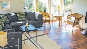 A modern living room with a sofa, a coffee table, wicker chairs, and a large window providing a view of the outdoors. - Stunning home in Risør with sauna (Risør)