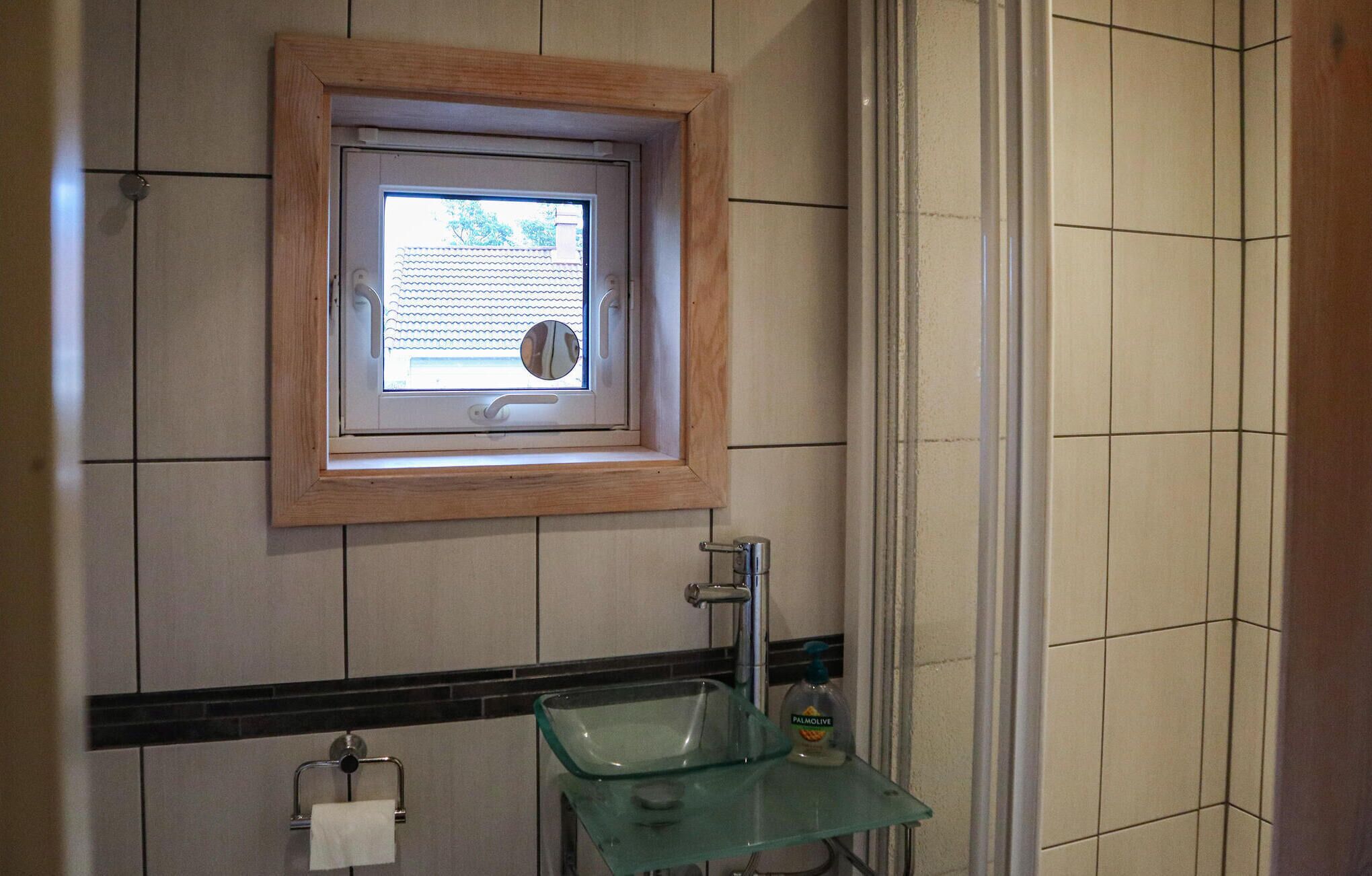 Ein Badezimmer mit einem Glaswaschbecken, einem Handtuchspender und einem Fenster mit Blick auf ein Gebäude.
