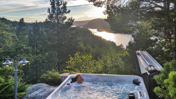 A hot tub with a person in it, surrounded by trees and overlooking a lake. - Stunning home in Risør with sauna (Risør)