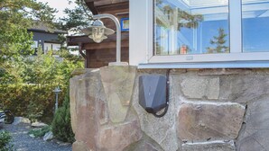 A stone wall with a mounted outdoor light fixture and a security camera. - Stunning home in Risør with sauna (Risør)