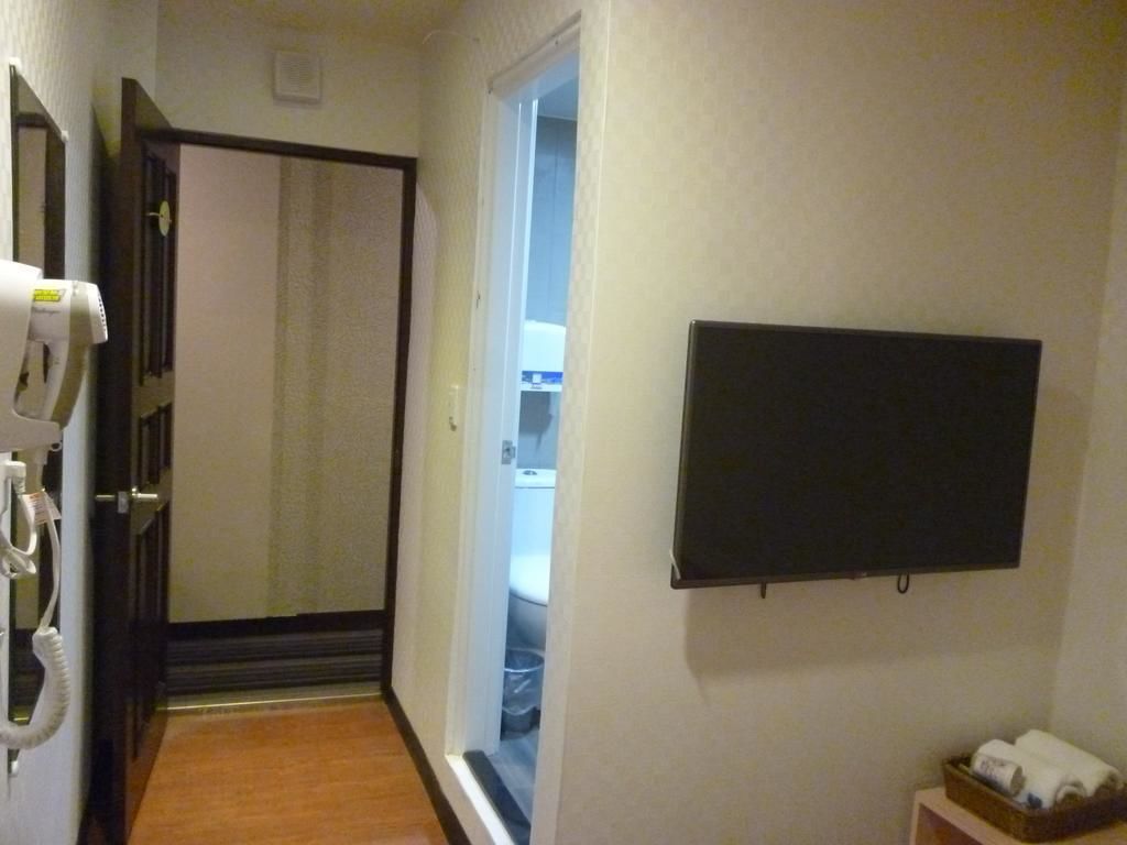Ein Flur mit einer zur Toilette führenden Tür, einem an der Wand befestigten Fernseher und einem kleinen Regal mit Handtüchern.