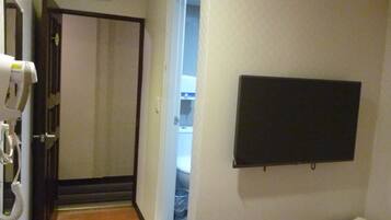 Ein Flur mit einer zur Toilette führenden Tür, einem an der Wand befestigten Fernseher und einem kleinen Regal mit Handtüchern.