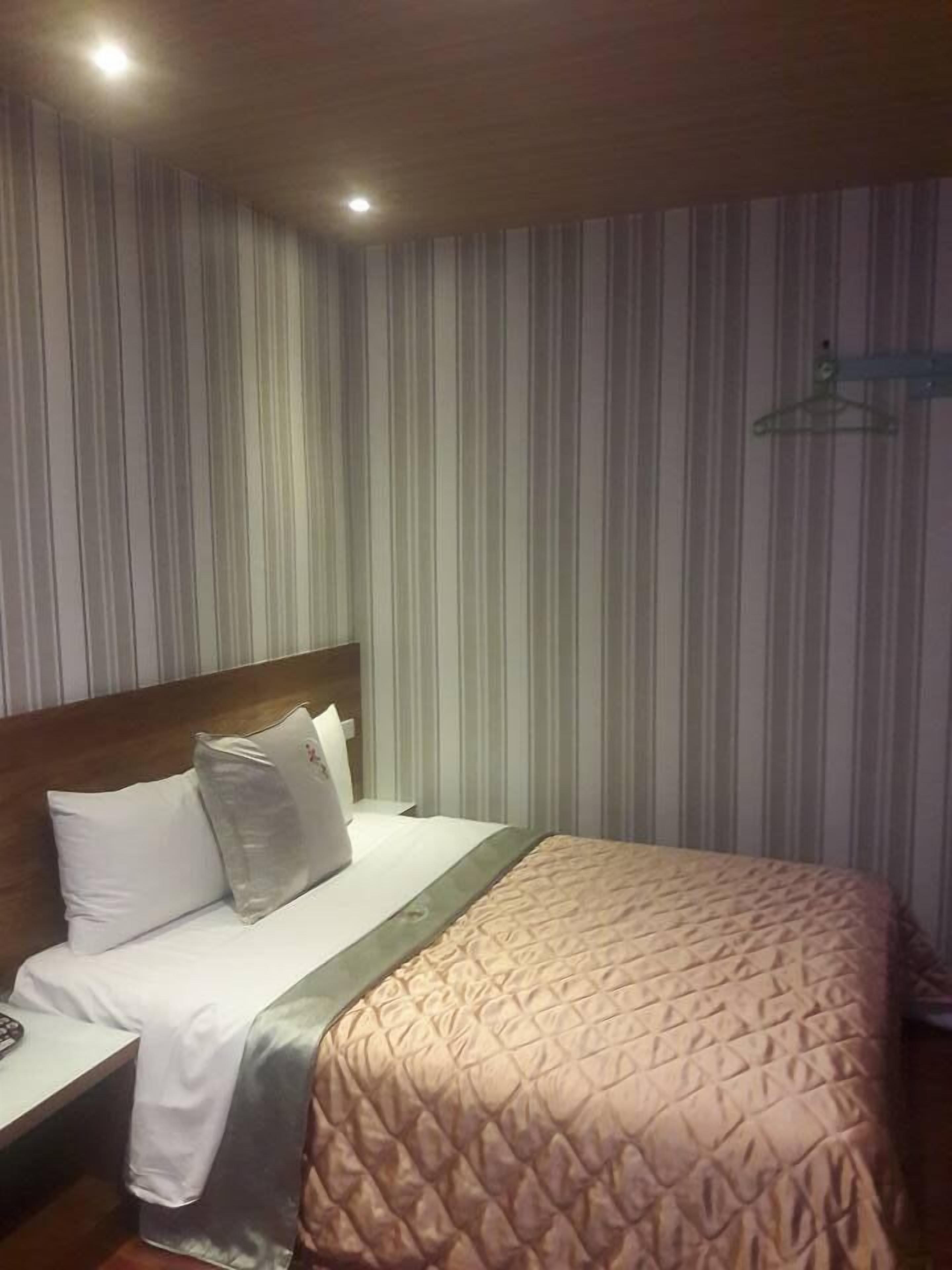 A hotel room with a striped wall, a bed with a quilted cover, a wooden headboard, and a hanging coat rack.