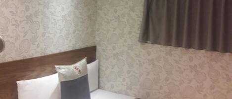 Habitación de hotel con cama, cabecero, aire acondicionado instalado en la pared y ventana con cortinas.