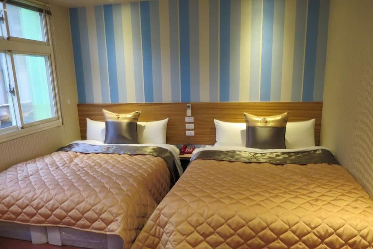 Two double beds with quilted covers, a striped wall, and a window with blinds.
