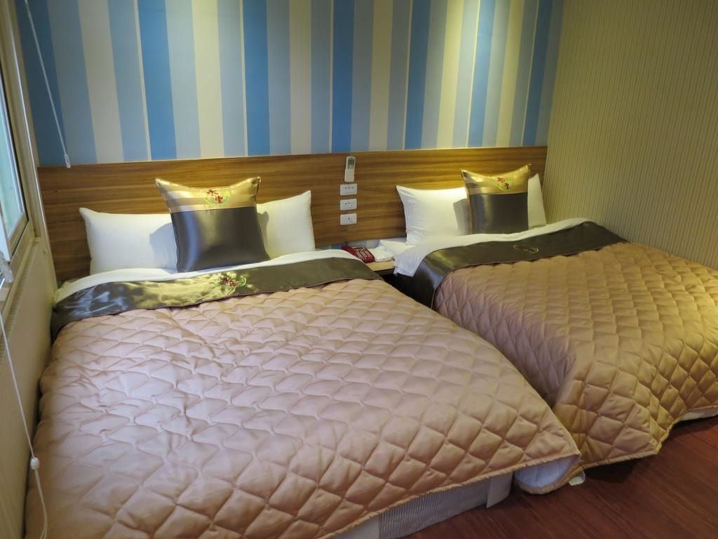 A hotel room with two beds, striped wallpaper, wooden headboard, and bedside lamps.