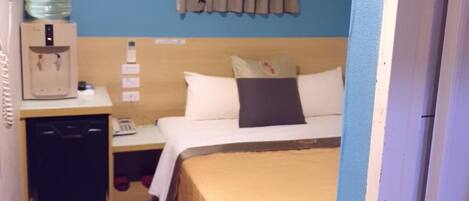 Habitación de hotel con cama, dispensador de agua, un pequeño escritorio con teléfono y aire acondicionado instalado en la pared.