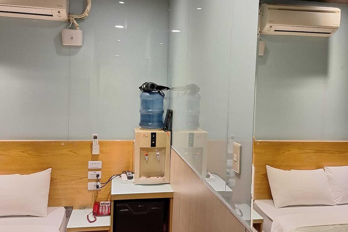 A hotel room with two beds, a small desk, a water dispenser, a phone, and a mirror.