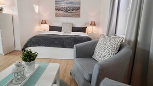 Ein modernes Schlafzimmer mit einem großen Bett, zwei Nachttischen mit Lampen, einem grauen Sofa, einer kleinen Topfpflanze und einem dekorativen Laternen.