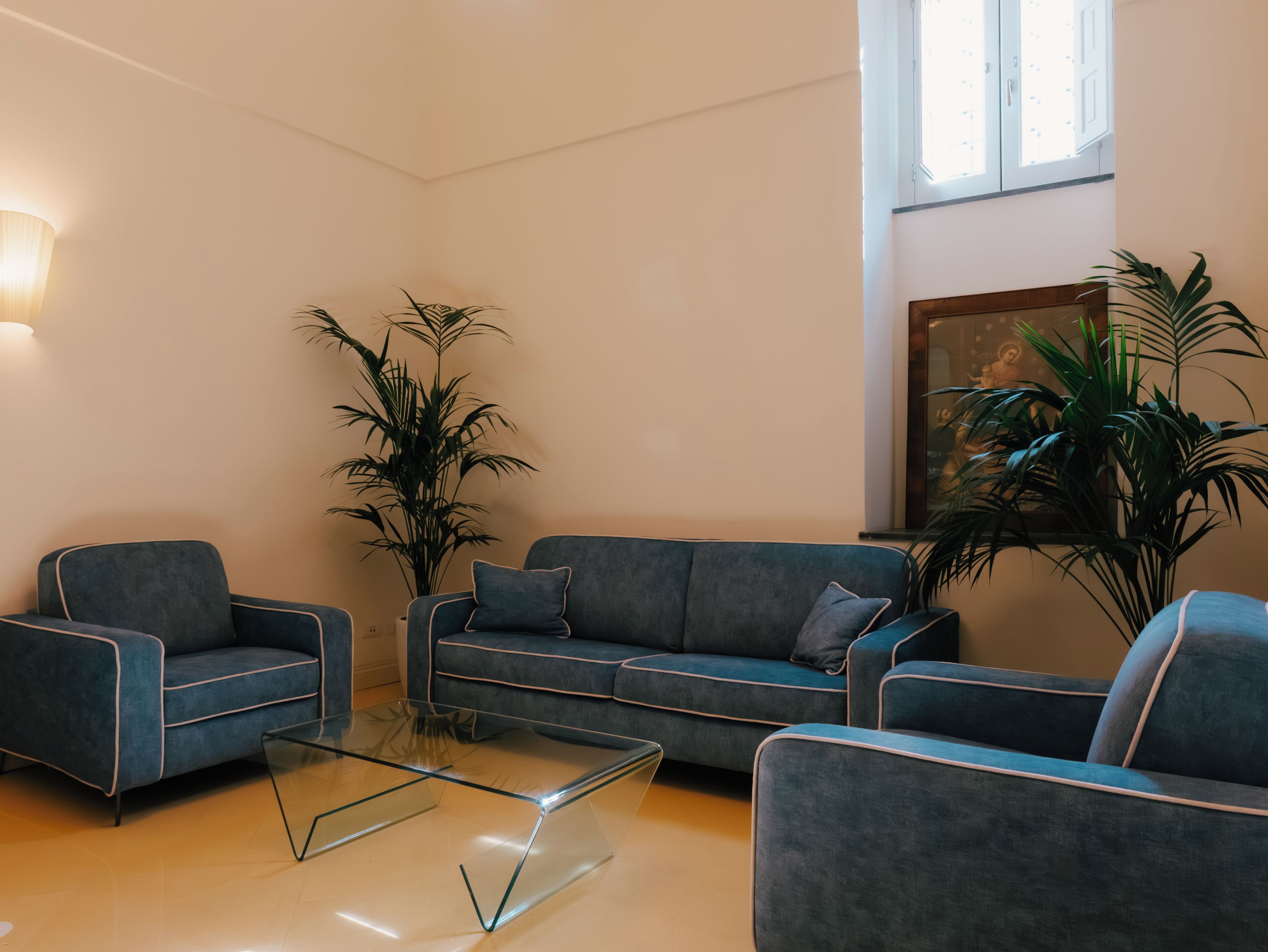 Un salon moderne avec un canapé, des fauteuils, une table basse en verre et des plantes en pot.