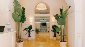 A hallway with potted plants, a reception desk, and a staircase leading to an upper level. - Unconventional Hotel Sorrento (Sant'Agnello)