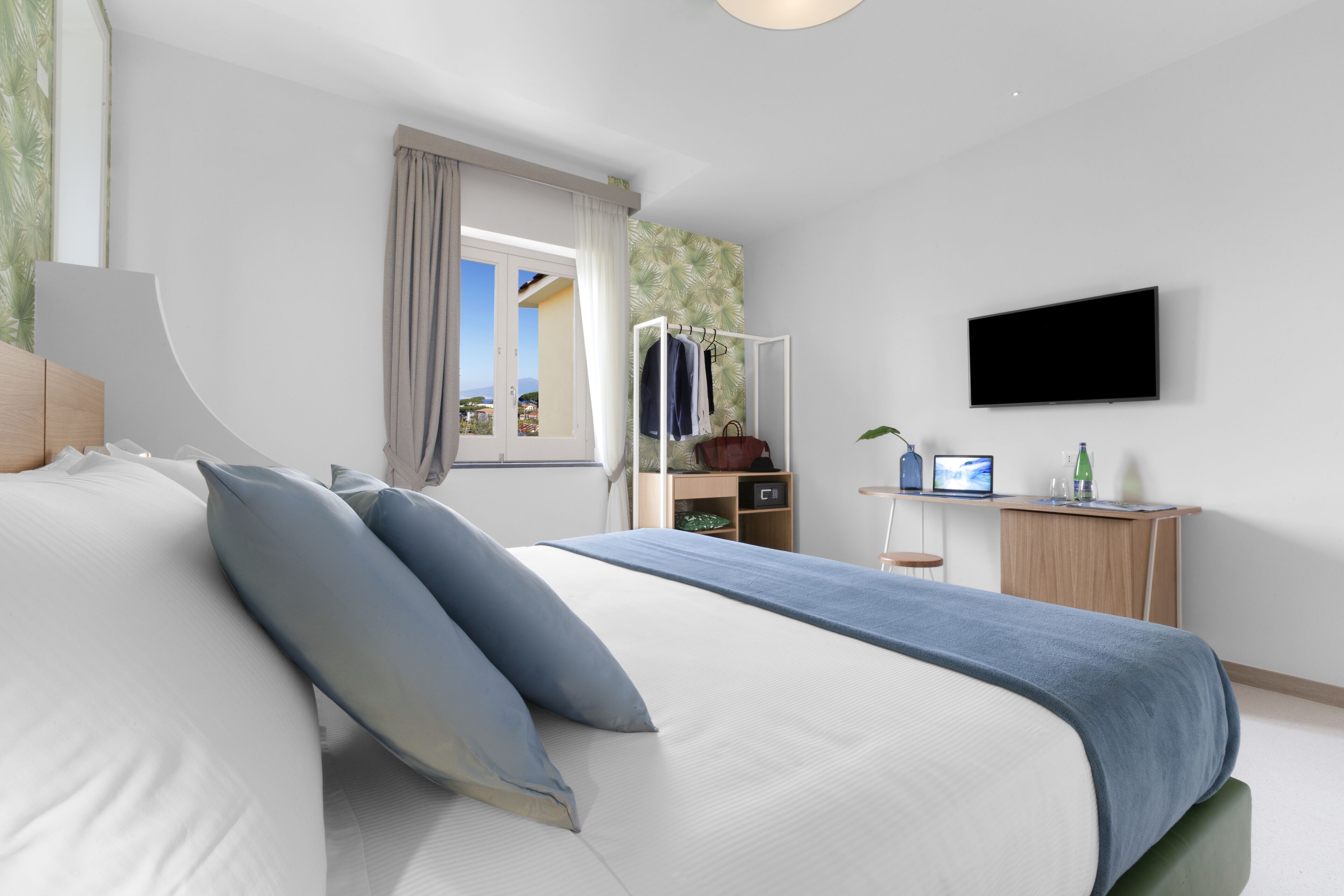 A modern bedroom with a bed, a desk, a TV, and a window with curtains.
