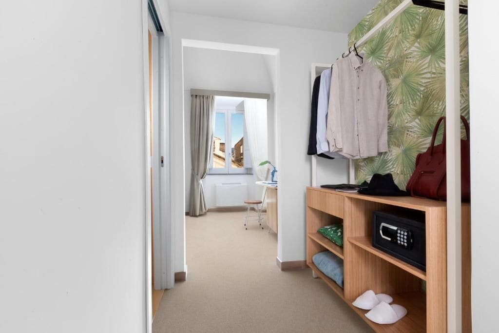 A hotel room with a wooden shelf, a microwave, and a view of the city through a window.