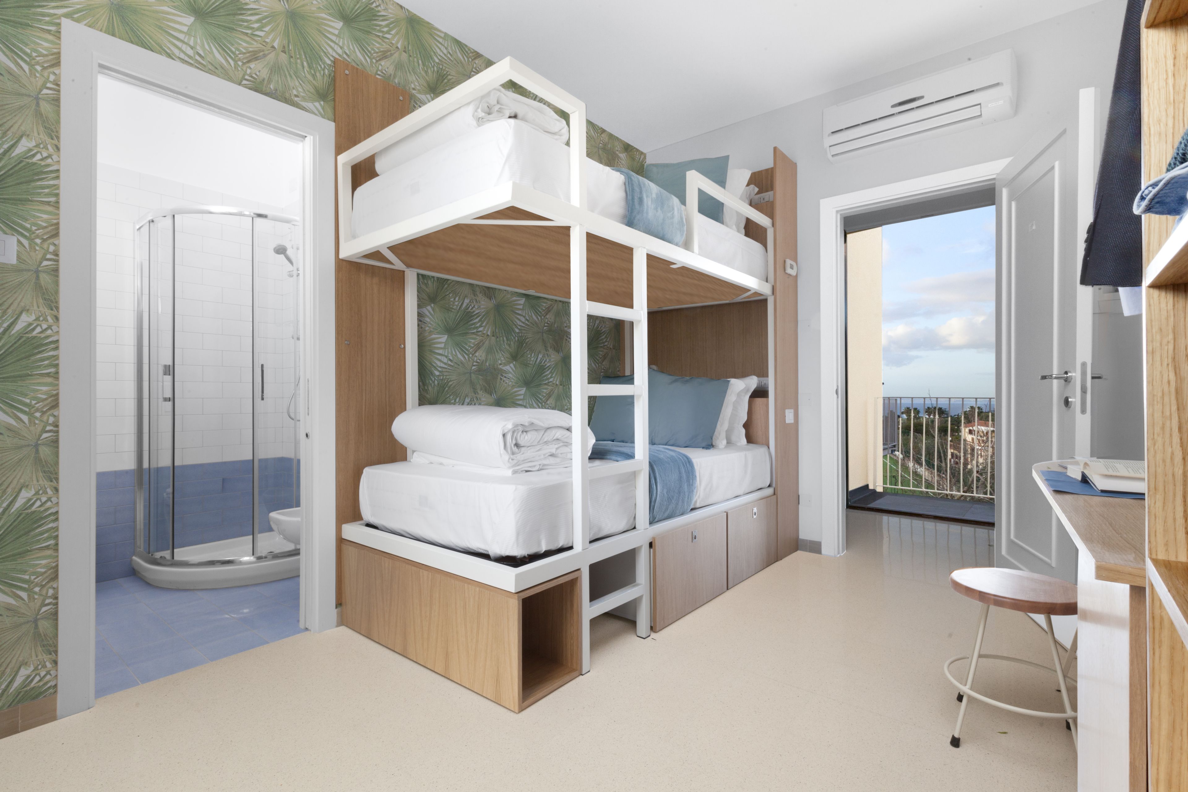 Ein Zimmer mit Etagenbetten, einer Dusche, einem Balkon mit Blick und einem kleinen Schreibtisch.
