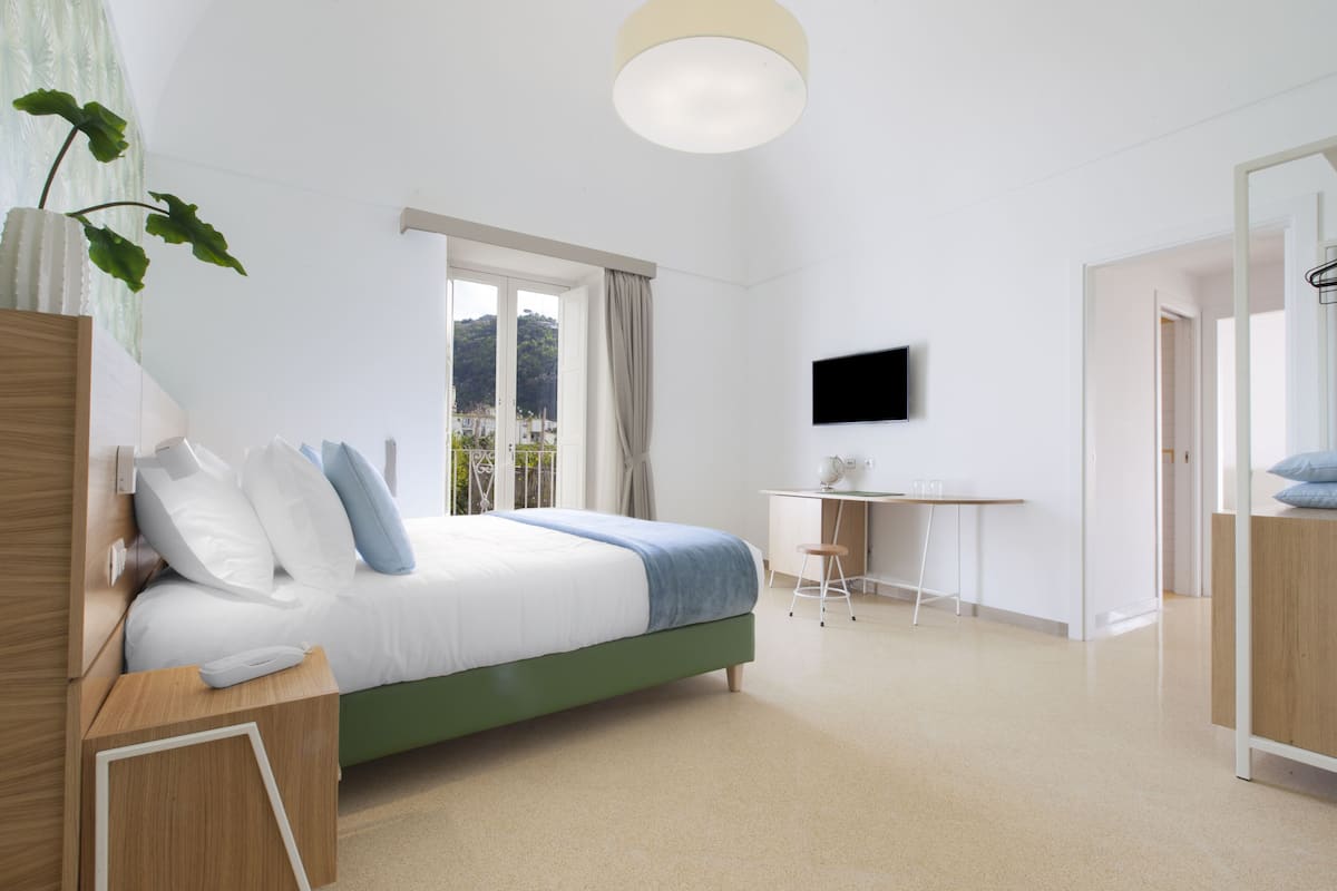 A modern bedroom with a bed, a desk, and a TV.