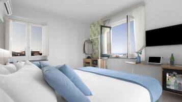 Habitación de hotel con una cama grande, un escritorio con una computadora portátil, un televisor montado en la pared y una ventana con cortinas.