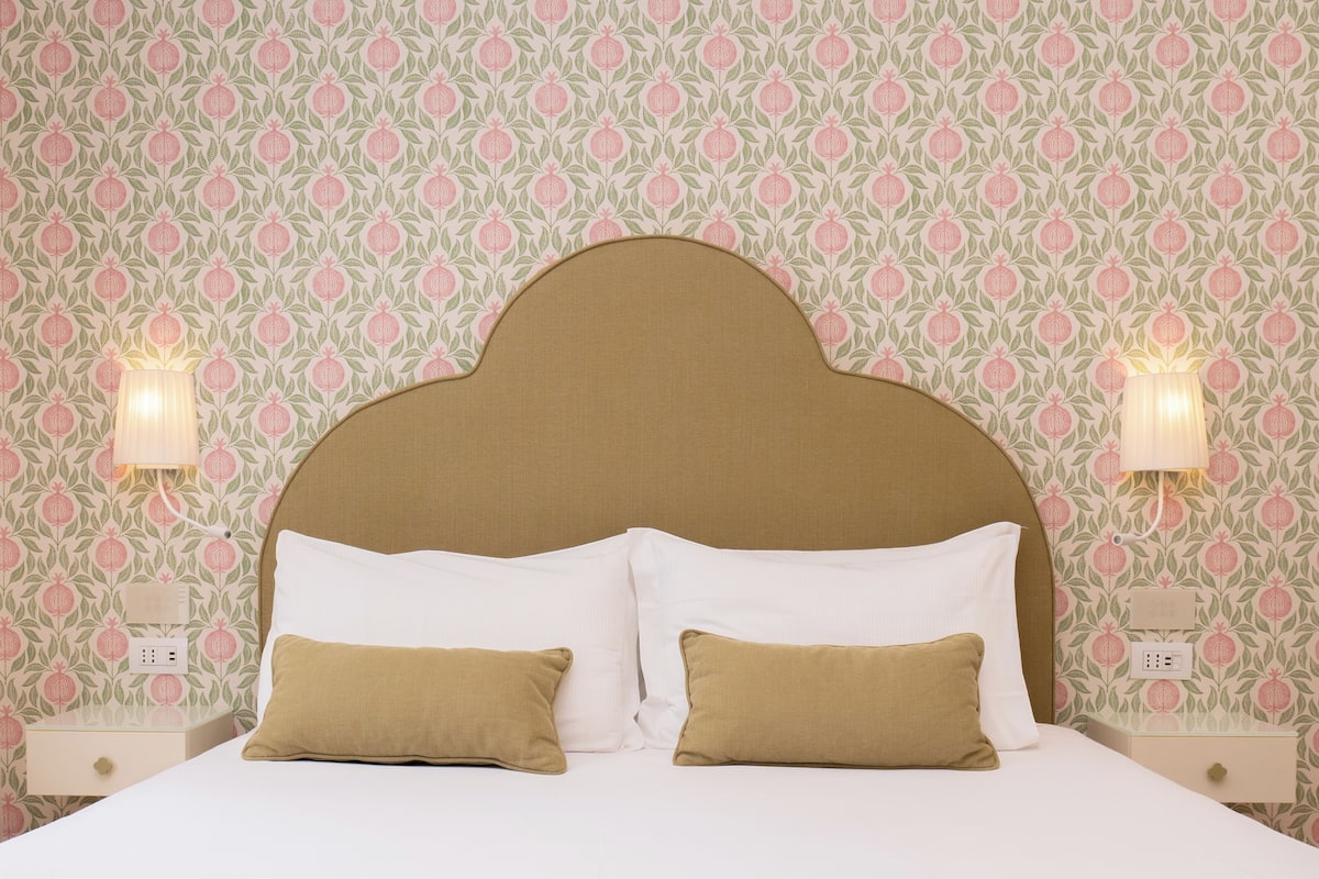 A bed with a headboard, two bedside lamps, and a nightstand with a power outlet.