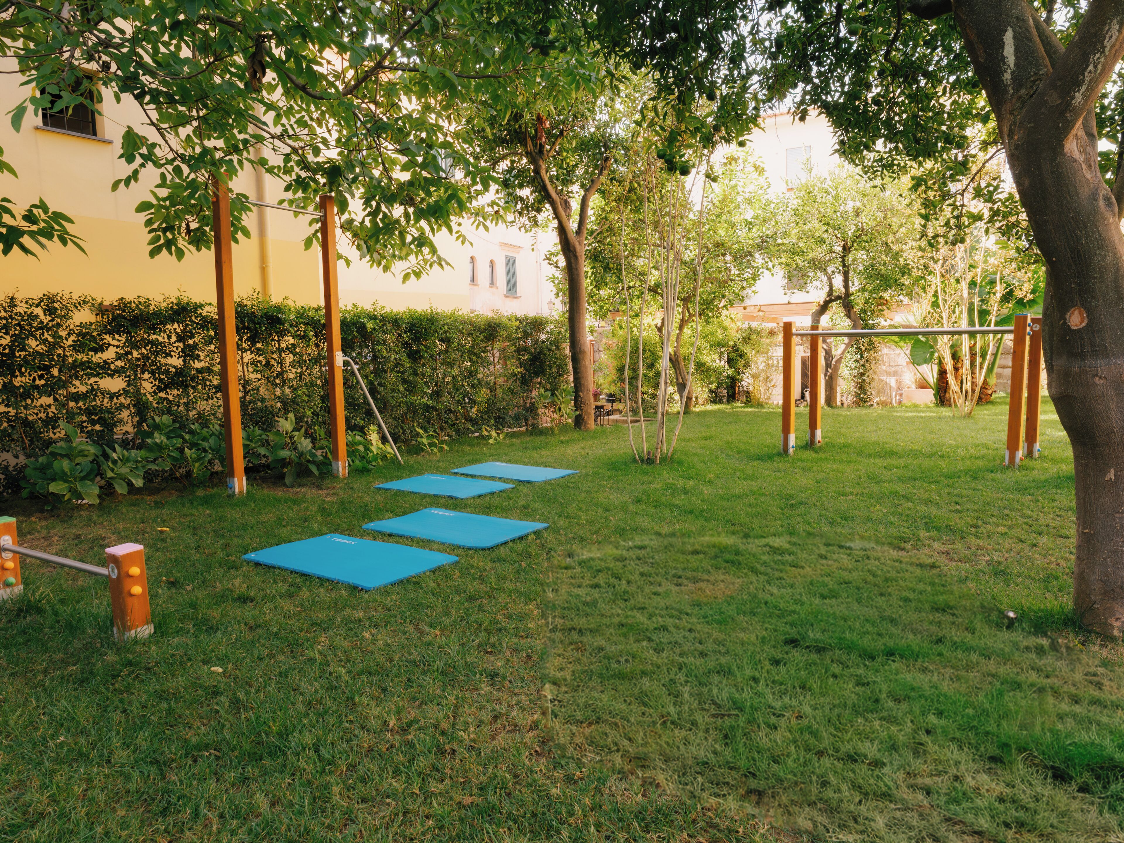 An outdoor area with exercise mats, a swing set, and a hedge.