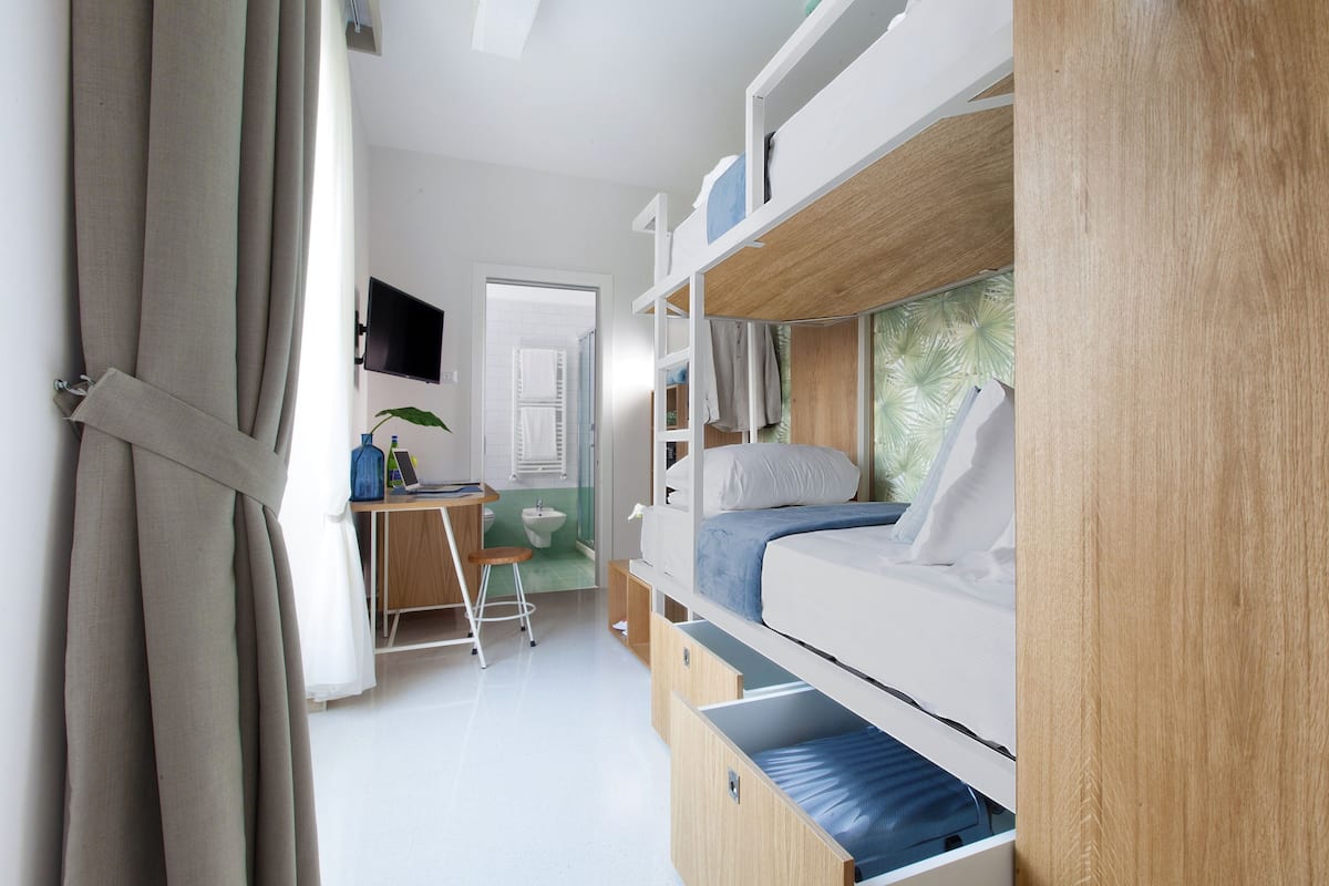 A compact room with bunk beds, a desk, and a small stool.