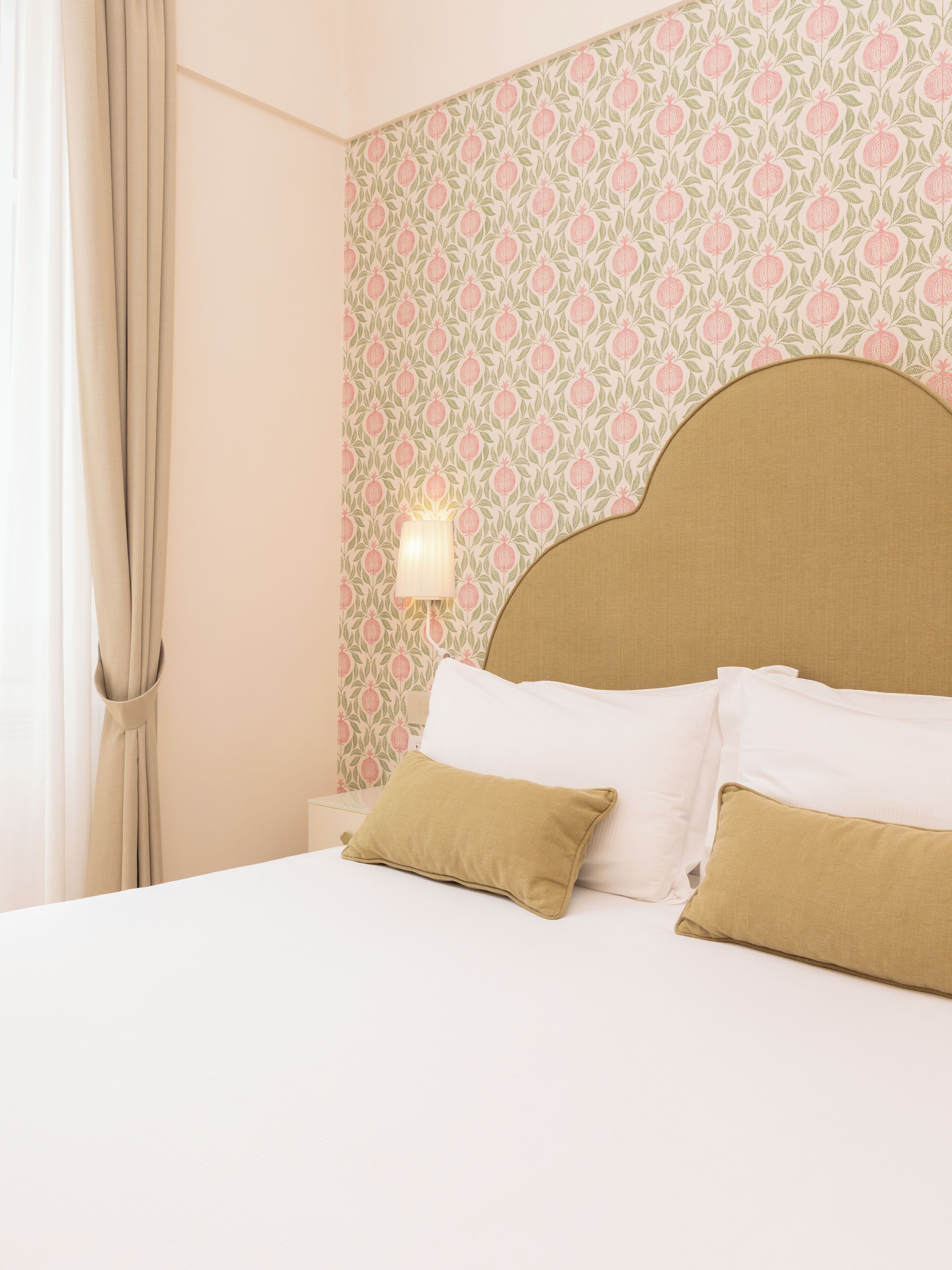 Een bed met wit en beige beddengoed, een hoofdbord en een muur met behang met een patroon.