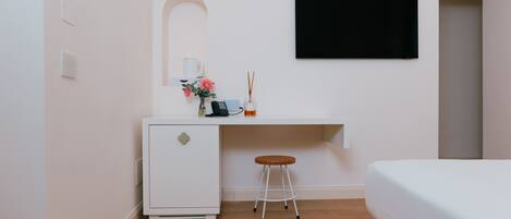 A compact hotel room with a bed, a small desk with a chair, a TV mounted on the wall, and a compact refrigerator.