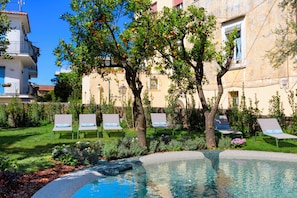 Zona de piscina con sillones reclinables y un árbol.
