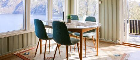 Un comedor con una mesa redonda, cuatro sillas, una lámpara colgante y vistas a un lago a través de amplios ventanales.