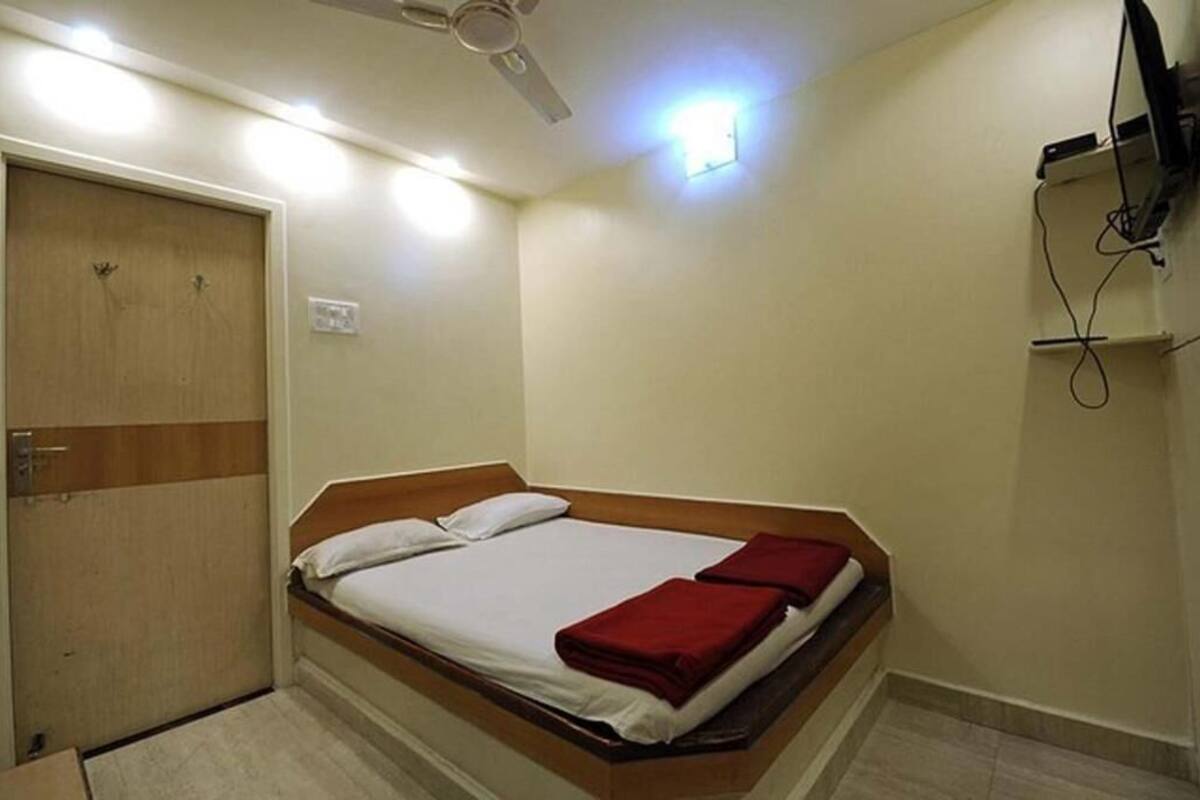 A single bed with a wooden headboard, a ceiling fan, a wall-mounted TV, and a door with a light switch.