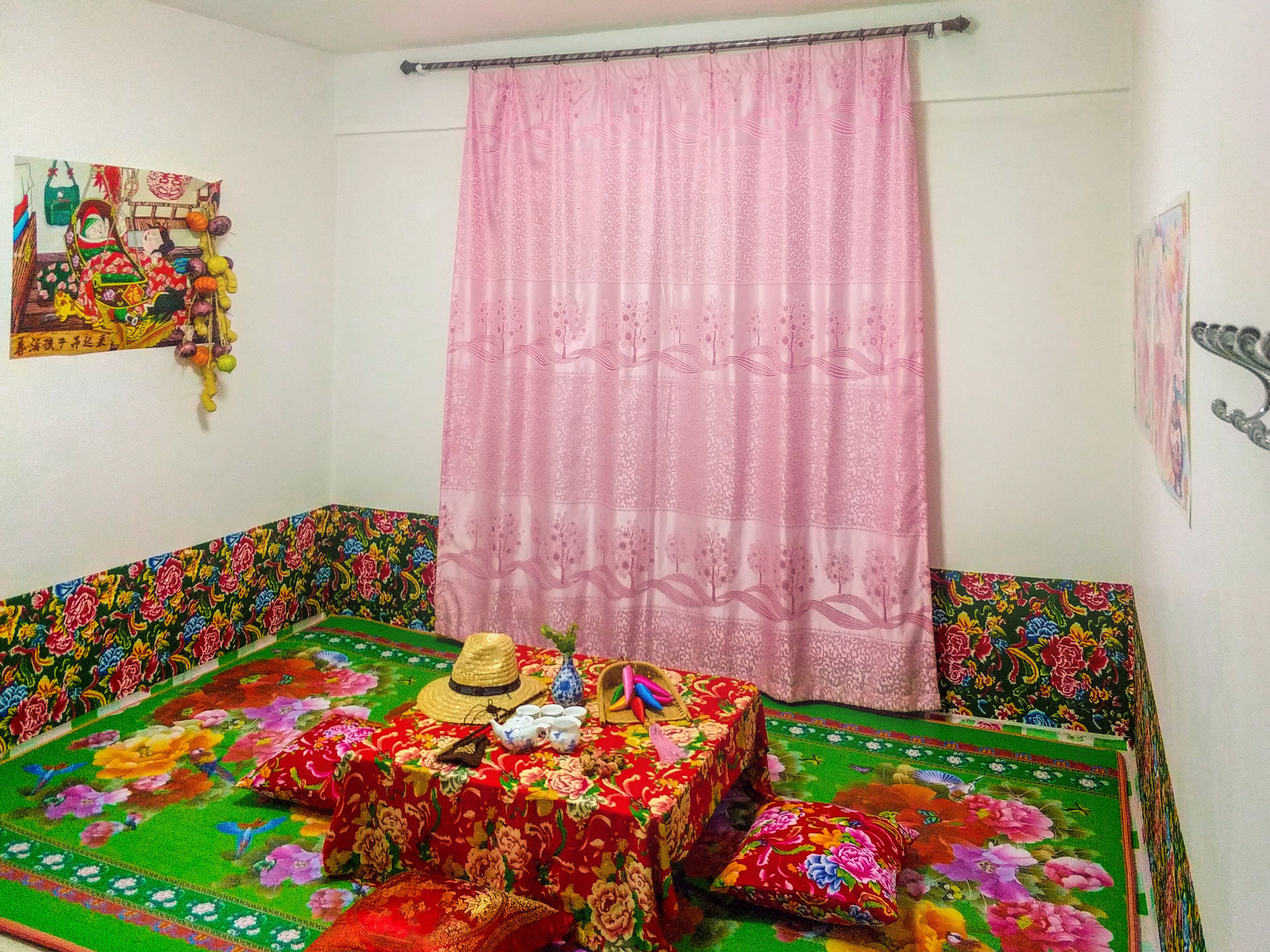 A room with a colorful bedspread, a pink curtain, and a wall hanging.