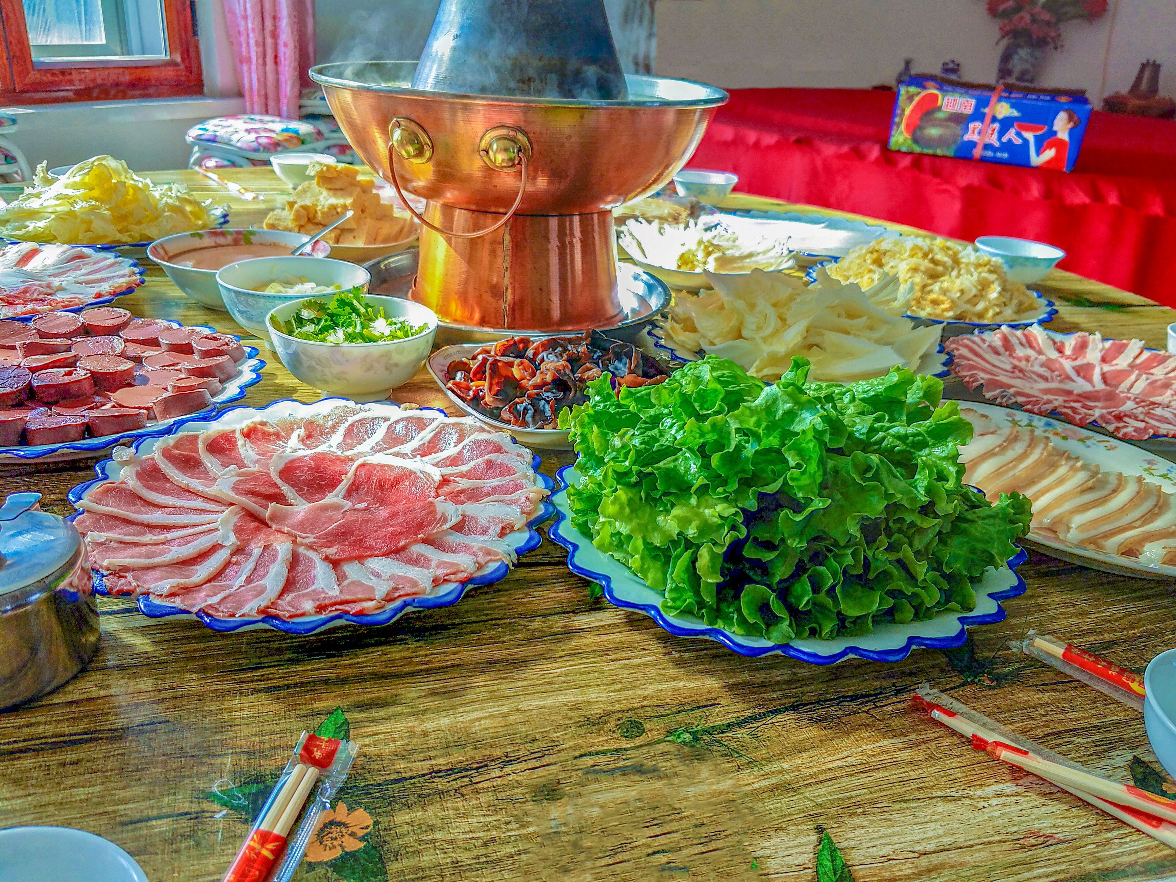 A table with various dishes, a copper hot pot, and chopsticks.