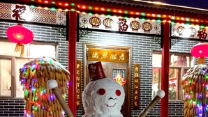 A snowman with a top hat and a sack, standing in front of a building with traditional Chinese architecture and illuminated signage.