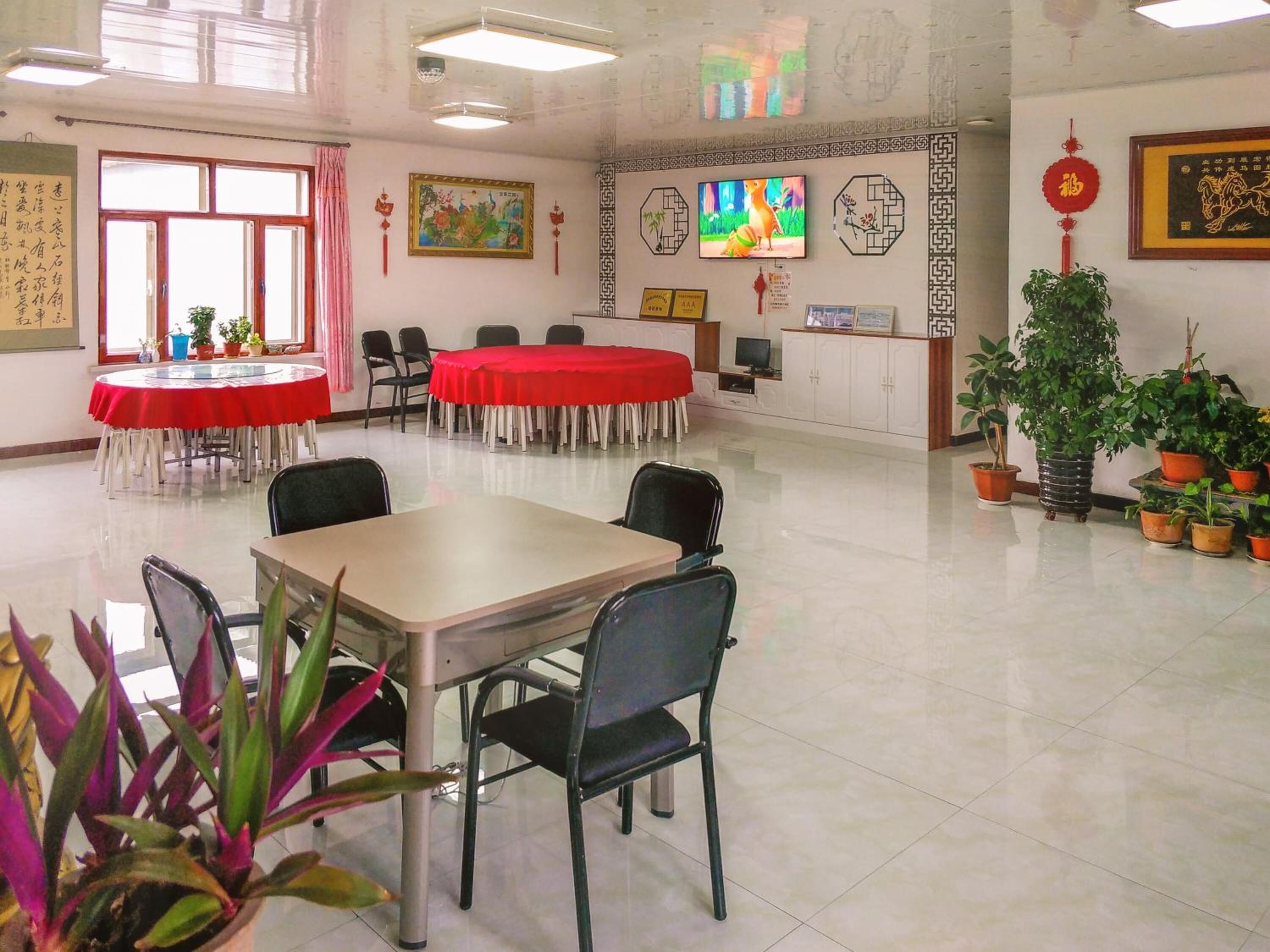 Un salón de conferencias con una mesa grande y sillas, una televisión y elementos decorativos como cuadros y plantas en macetas.