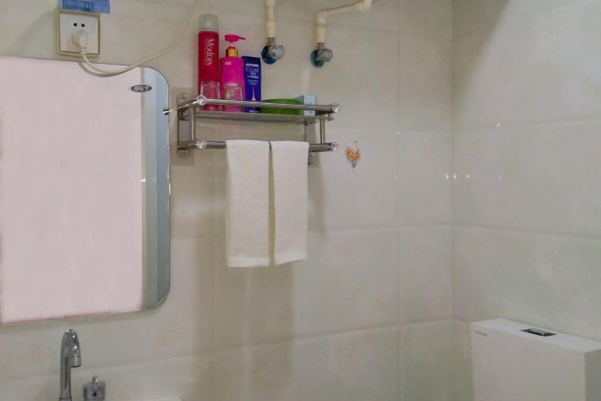 A bathroom with a white sink, a mirror, a towel rack with two white towels, and toiletries on a shelf.