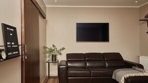 A modern living room with a leather sofa, a flat-screen TV, a small side table with a plant, and a wall-mounted welcome sign. - Keflavik Micro Suites (Reykjanesbær)