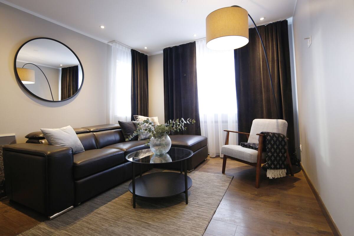 A modern living room with a black leather sofa, a round coffee table, and a round mirror on the wall.